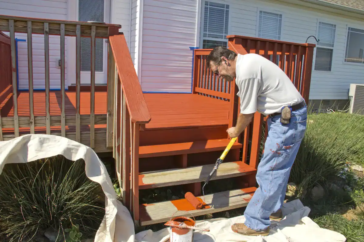 Contractor applying deck stain to wooden stairs with a brush
